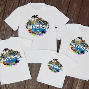 May include: White t-shirts with the Universal Studios logo, featuring a colourful graphic of characters and the word "UNIVERSAL". The shirts are displayed on a wooden surface.