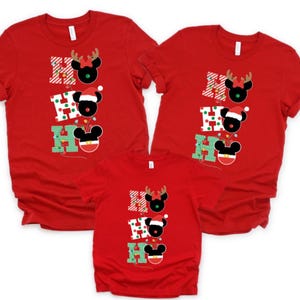 May include: Red t-shirts with a Christmas design. Each shirt displays "HO HO HO" with Mickey Mouse-inspired characters. The design includes reindeer antlers, Santa hats, and festive lights. A family set of matching shirts.
