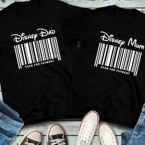 以下が含まれることがあります： 白い文字とバーコードが付いた黒いTシャツが2枚。左側のTシャツには「Disney Dad」、右側のTシャツには「Disney Mum」と書いてあります。両方のTシャツにはバーコードの下に「Scan for Payment」と書いてあります。