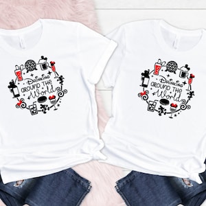 May include: Two white t-shirts with a black and red design featuring the text "Drinking around the world" and various Disney icons, including Mickey Mouse, the Epcot ball, and drinks.