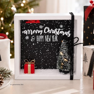 Könnte beinhalten: Ein weißer quadratischer Schattenfugenrahmen mit schwarzem Hintergrund, weißen Schneeflockenmustern und dem Text Merry Christmas & Happy New Year. Darin befinden sich ein kleines rotes Geschenk mit goldener Schleife und ein beleuchteter Mini-Tannenbaum.