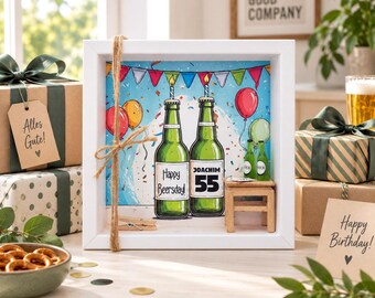 May include: A white shadow box frame containing a birthday illustration of two green beer bottles with candles, balloons, and bunting. The bottles feature the text Happy Beersday and Joachim 55. A small wooden stool and two miniature bottles are included.