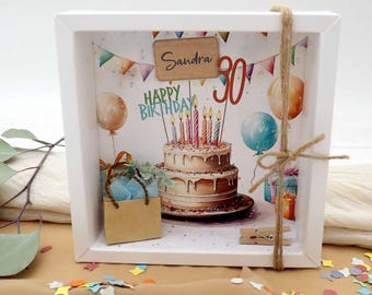 Könnte beinhalten: Ein weißer Schattenrahmen mit Geburtstagsthema. Das Kunstwerk zeigt eine zweistöckige Torte mit Kerzen, Luftballons und dem Text "Happy Birthday". Der Name "Sandra" und die Zahl "30" sind ebenfalls abgebildet. Ein kleiner Geschenkebeutel und Geschenke sind enthalten.