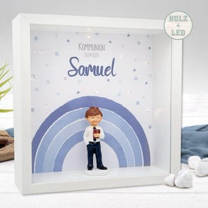 Könnte beinhalten: Ein weißer Schattenrahmen mit einem blauen Regenbogen-Design und einer Figur eines Jungen, der ein Buch hält. Die Box trägt den Namen "Samuel" und das Wort "Kommunion". Die Box ist mit kleinen LED-Leuchten beleuchtet.