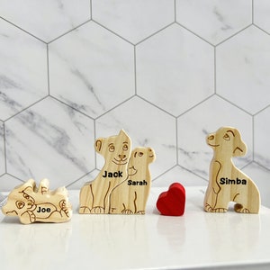 Puede incluir: Cuatro figuritas de le&oacute;n de madera con los nombres "Joe", "Jack", "Sarah" y "Simba" grabados en ellas. Un coraz&oacute;n rojo se coloca entre las figuritas.