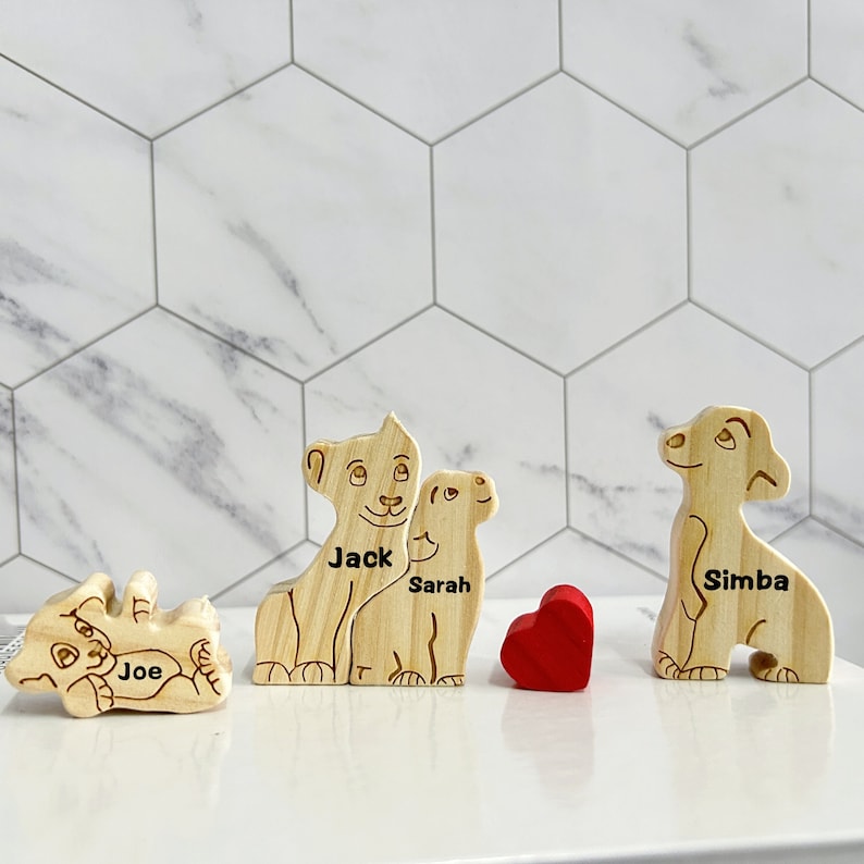 Puede incluir: Cuatro figuritas de le&oacute;n de madera con los nombres "Joe", "Jack", "Sarah" y "Simba" grabados en ellas. Un coraz&oacute;n rojo se coloca entre las figuritas.