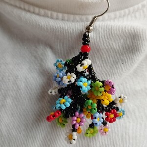 May include: A single beaded earring with a cluster of colorful flowers. The flowers are made of small, round beads in shades of blue, green, yellow, pink, red, and white. The earring is attached to a silver hook.