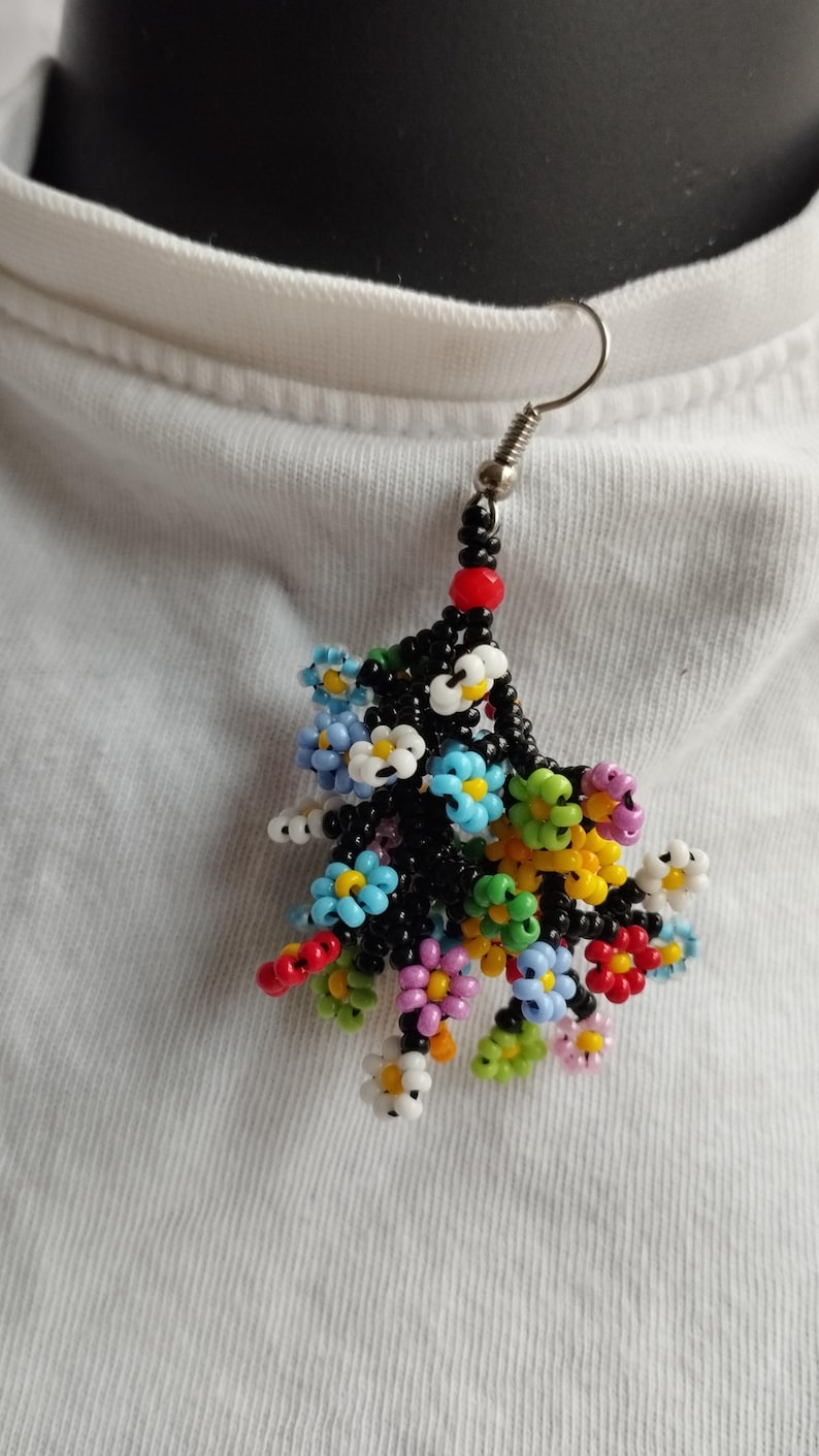 May include: A single beaded earring with a cluster of colorful flowers. The flowers are made of small, round beads in shades of blue, green, yellow, pink, red, and white. The earring is attached to a silver hook.
