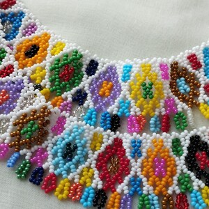 May include: A colorful beaded necklace with a geometric pattern. The necklace features a variety of colors including white, yellow, green, blue, red, and purple. The beads are arranged in a repeating pattern, creating a vibrant and eye-catching design.