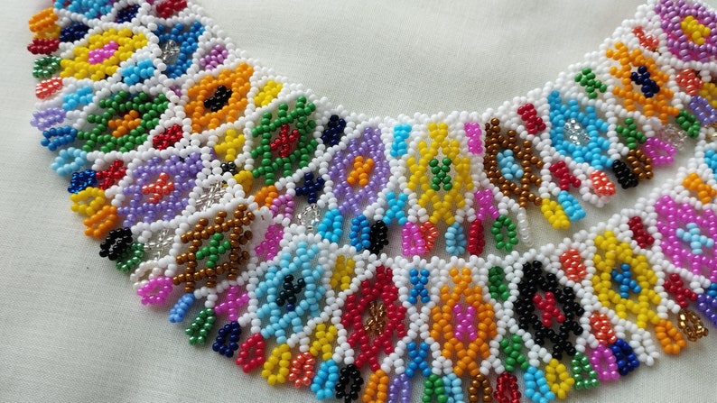 May include: A colorful beaded necklace with a geometric pattern. The necklace features a variety of colors including white, yellow, green, blue, red, and purple. The beads are arranged in a repeating pattern, creating a vibrant and eye-catching design.