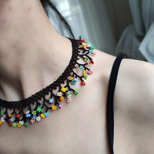 May include: A black beaded necklace with colorful flower accents. The necklace is made of small black beads and features a delicate floral design with colorful beads.