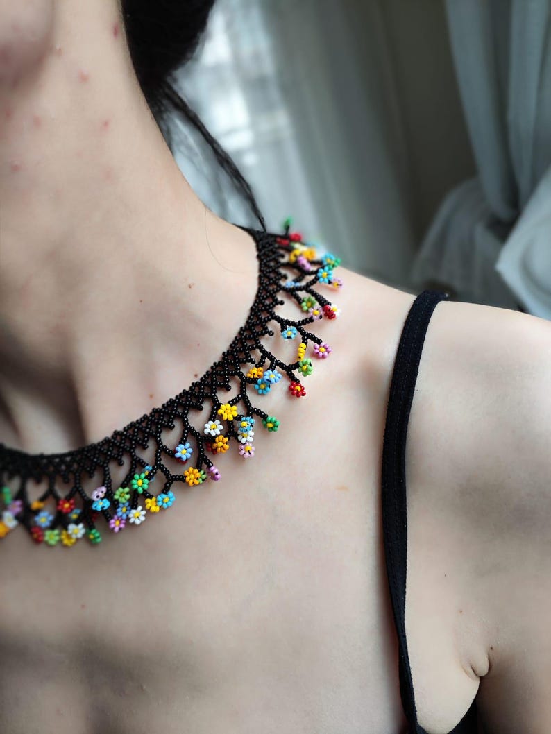 May include: A black beaded necklace with colorful flower accents. The necklace is made of small black beads and features a delicate floral design with colorful beads.