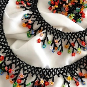 May include: A black beaded necklace with colorful flower accents. The necklace has a fringe design with small, colorful flowers hanging from the bottom. The necklace is paired with matching earrings.