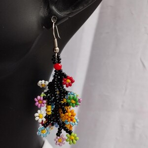 May include: A pair of dangle earrings with a cluster of colorful beaded flowers hanging from black beaded stems. The earrings are silver and have a hook closure.