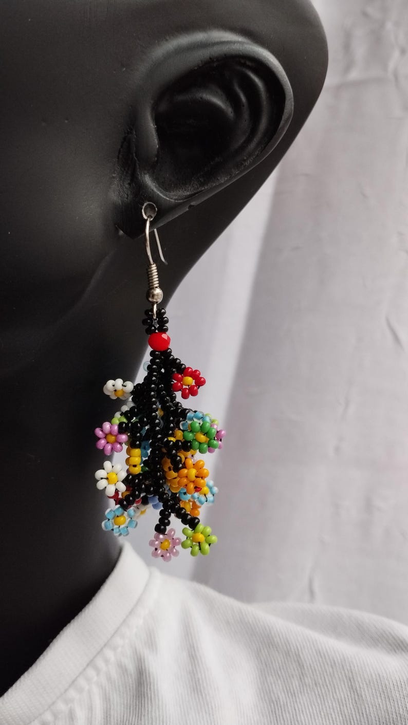 May include: A pair of dangle earrings with a cluster of colorful beaded flowers hanging from black beaded stems. The earrings are silver and have a hook closure.