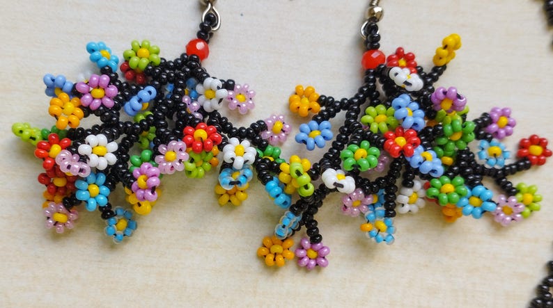 May include: A pair of dangle earrings with black beaded branches and colorful flower-shaped beads. The flowers are made of small, colorful beads in various shades of pink, blue, green, yellow, red, and white.