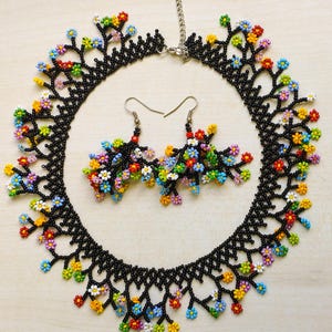 May include: A black beaded necklace and matching earrings with colorful flower accents. The necklace is a delicate chain with a floral design and the earrings are small and dangle.