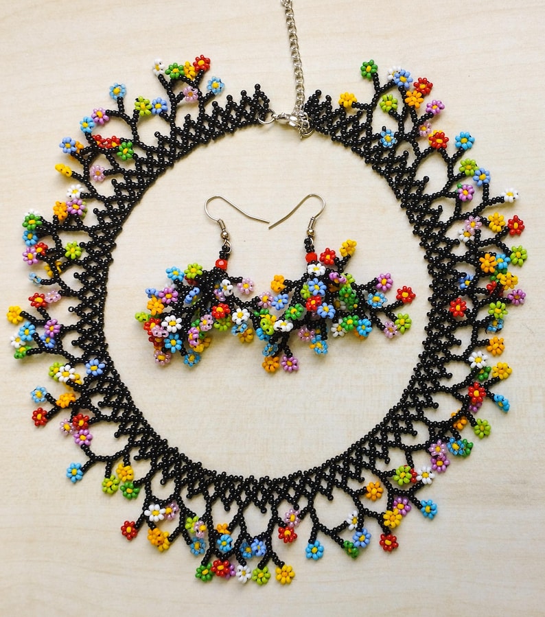 May include: A black beaded necklace and matching earrings with colorful flower accents. The necklace is a delicate chain with a floral design and the earrings are small and dangle.