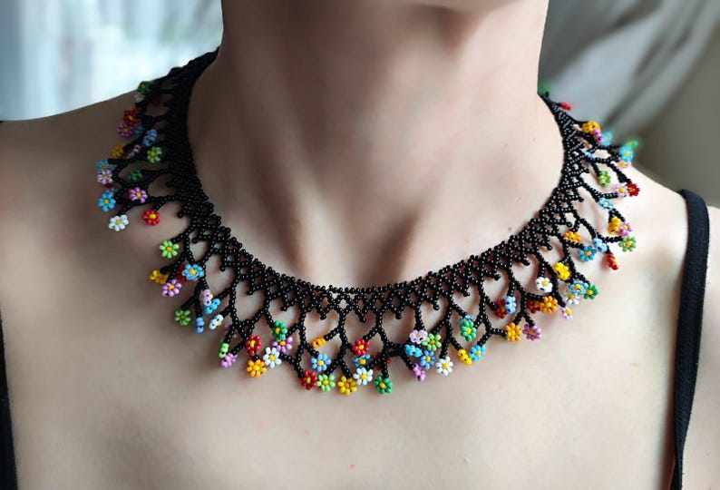 May include: A black beaded necklace with a delicate floral design. The flowers are made of colorful beads and are arranged in a cascading pattern.