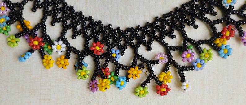 May include: A black beaded necklace with colorful flower-shaped beads. The necklace has a delicate, intricate design with dangling flower accents.