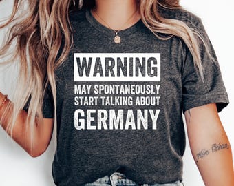 Puede incluir: Una camiseta gris oscuro con texto blanco que dice "WARNING MAY SPONTANEOUSLY START TALKING ABOUT GERMANY".