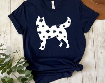 Può includere: Una maglietta blu navy con una silhouette bianca di un cane husky. Il cane è ricoperto da un motivo di fiori bianchi.