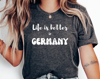 May include: A dark gray t-shirt with white text that reads "Life is better in GERMANY". The text is in a wavy font.