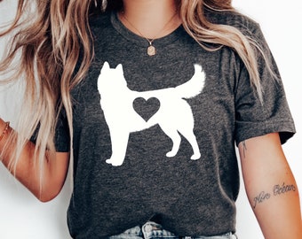 Op de afbeelding: Een donkergrijs T-shirt met een wit silhouet van een husky-hond met een hart op zijn borst. Het shirt wordt gedragen door een persoon met lang blond haar.