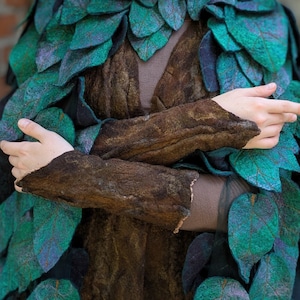 May include: A person wearing a green and blue leaf-shaped costume with a brown felt base. The costume is made of felt and has a crown of leaves on their head.