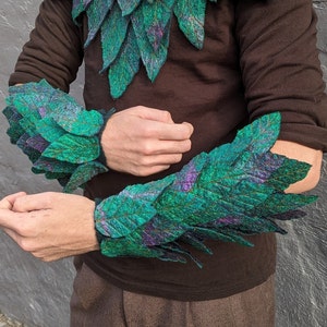 May include: A pair of green and purple felt arm warmers with a leaf design. The arm warmers are made of felt and have a textured surface.