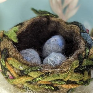May include: A brown, green and orange yarn bird's nest with three blue eggs inside.