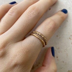 Op de afbeelding: Twee gouden ringen aan een vinger. De bovenste ring heeft een getextureerd oppervlak en de onderste ring is glad.