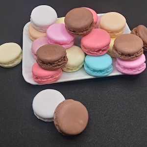Può includere: Una varietà di macarons colorati su un piatto bianco. I macarons sono disposti in cerchio con i colori rosa, blu, marrone e bianco.