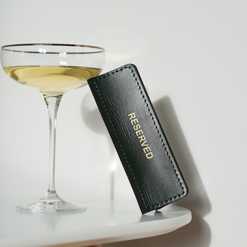 May include: A green leather table card with gold lettering that reads "RESERVED".