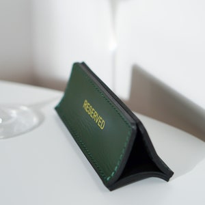 May include: A green leather table sign with gold lettering that reads "RESERVED".