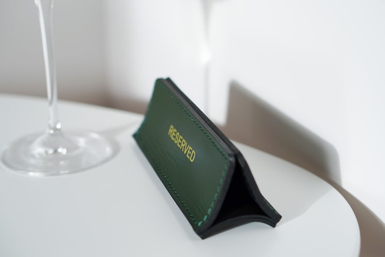 May include: A green leather table sign with gold lettering that reads "RESERVED".