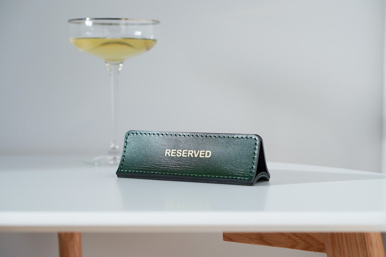 May include: A green leather table sign with gold lettering that reads "RESERVED".