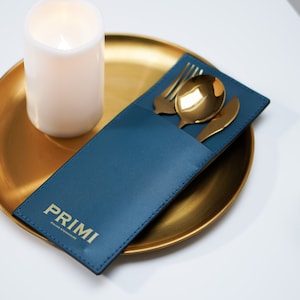 May include: A blue leather cutlery pouch with gold lettering that says "PRIMI" on a gold tray with a white candle.