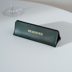 May include: A green leather table sign with gold lettering that reads "RESERVED".
