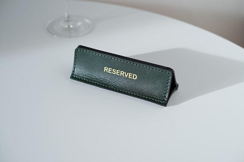 May include: A green leather table sign with gold lettering that reads "RESERVED".