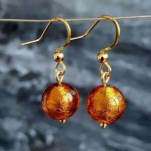 May include: A pair of gold earrings with amber glass beads. The beads have a metallic gold finish.