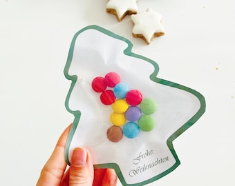 May include: A festive image showing a tree-shaped package filled with colourful sweets. The package has a green border and the text "Frohe Weihnachten". Two pine cones and star-shaped biscuits are also visible.