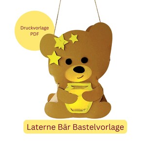 Könnte beinhalten: Eine braune Papierlaterne in Form eines Teddybären, der ein gelbes Glas hält. Der Bär hat schwarze Augen und einen lächelnden Mund. Gelbe Sterne schmücken den Kopf des Bären. Der Text auf dem Bild lautet "Druckvorlage PDF" und "Laterne Bär Bastelvorlage".