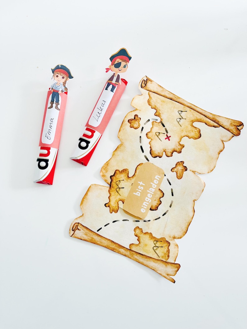 Puede incluir: Dos barras de caramelo rosa y rojo con personajes de piratas en la parte superior. Las barras de caramelo est&aacute;n etiquetadas con "du" y tienen los nombres "Emma" y "Lucas" escritos en ellas. Un mapa del tesoro marr&oacute;n y blanco con una X roja y el texto "bist eingeladen" est&aacute; en el fondo.