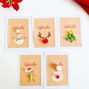 Könnte beinhalten: Fünf Weihnachtskarten mit dem deutschen Satz "Frohe Weihnachten" aufgedruckt. Jede Karte zeigt ein anderes festliches Design: einen Schneemann, ein Rentier, einen Weihnachtsbaum, einen Lebkuchenmann und den Weihnachtsmann.