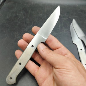 Könnte beinhalten: Eine einfache, silberne Messerklinge mit einem abgerundeten Griff und drei Löchern. Die Klinge wird in einer Hand gehalten.