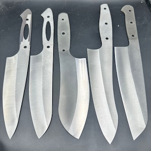 Könnte beinhalten: Fünf silberfarbene Messerklingen in verschiedenen Formen und Größen. Die Klingen liegen auf einer dunkelgrauen Oberfläche.