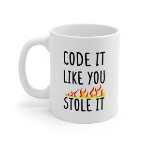 Puede incluir: Taza de café de cerámica blanca con texto negro que dice "CODE IT LIKE YOU STOLE IT" con un gráfico de llama naranja y amarillo estilizado debajo del texto.