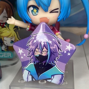 Puede incluir: Un botón en forma de estrella con un fondo morado que presenta una ilustración de personaje con cabello morado, una máscara facial negra y una chaqueta azul y blanca. Estrellas blancas están dispersas alrededor de los bordes. Una figura con cabello azul está en el fondo.