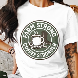Könnte beinhalten: Weißes T-Shirt mit einem kreisförmigen Design mit dem Text "FARM STRONG COFFEE STRONGER". Das Design zeigt eine dampfende Kaffeetasse, einen Cowboy-Stiefel und ein Seil. Das T-Shirt ist ein Freizeitkleidungsstück.
